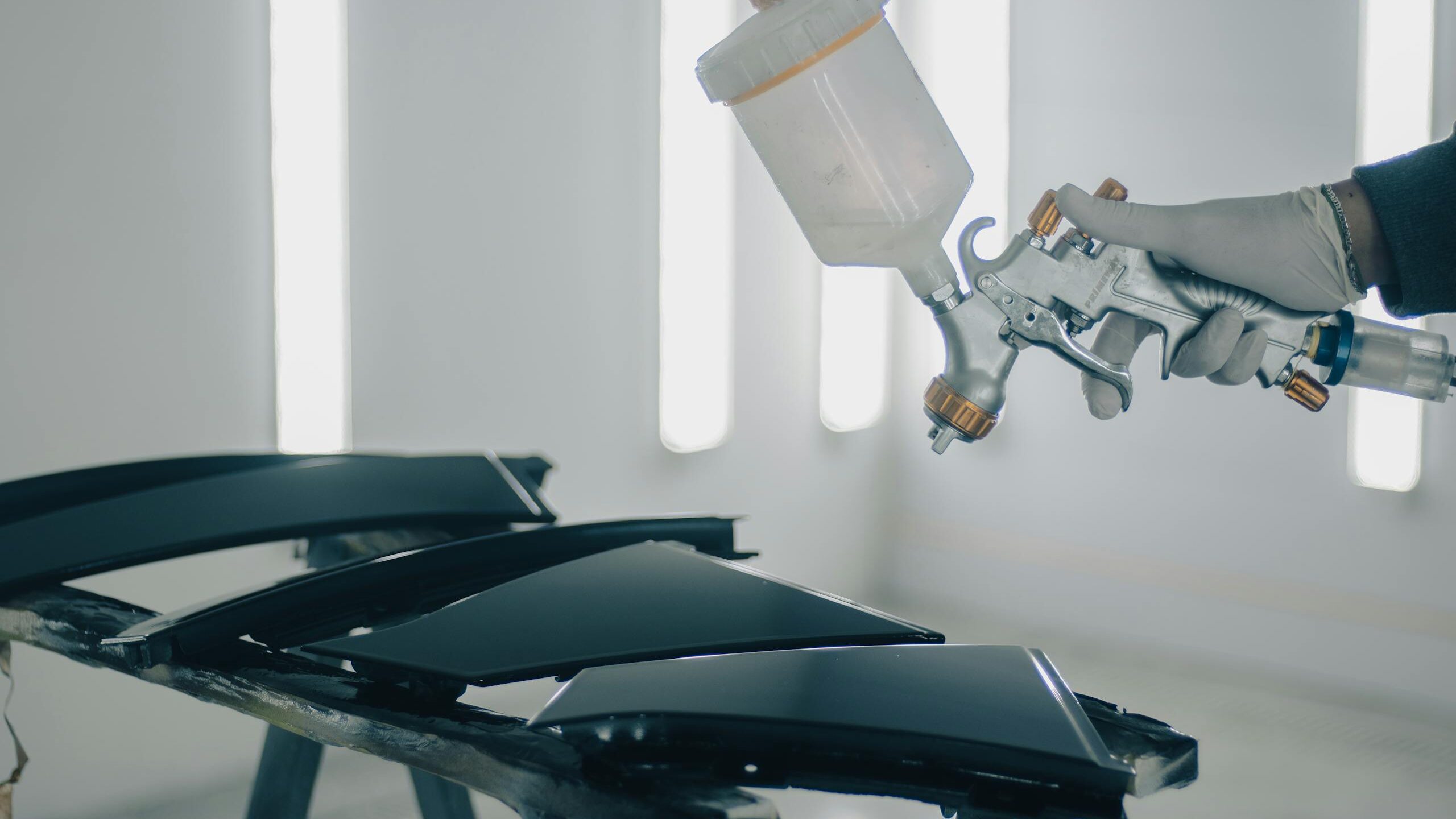 Close-up of car parts being spray-painted in an automotive workshop.
