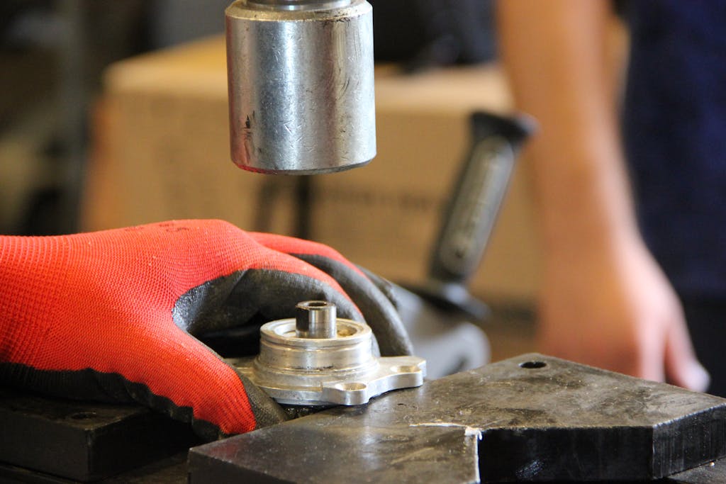 Hands in red gloves operate metal machinery in workshop close-up.