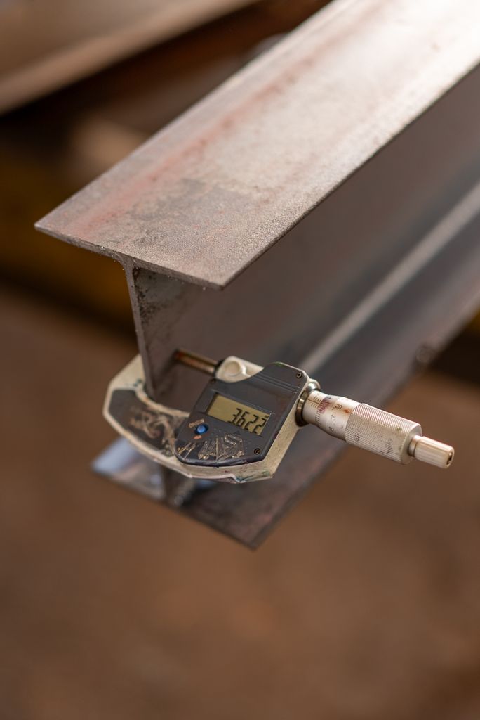 Profile Close-up of an industrial caliper measuring the thickness of a steel beam in a workshop.
