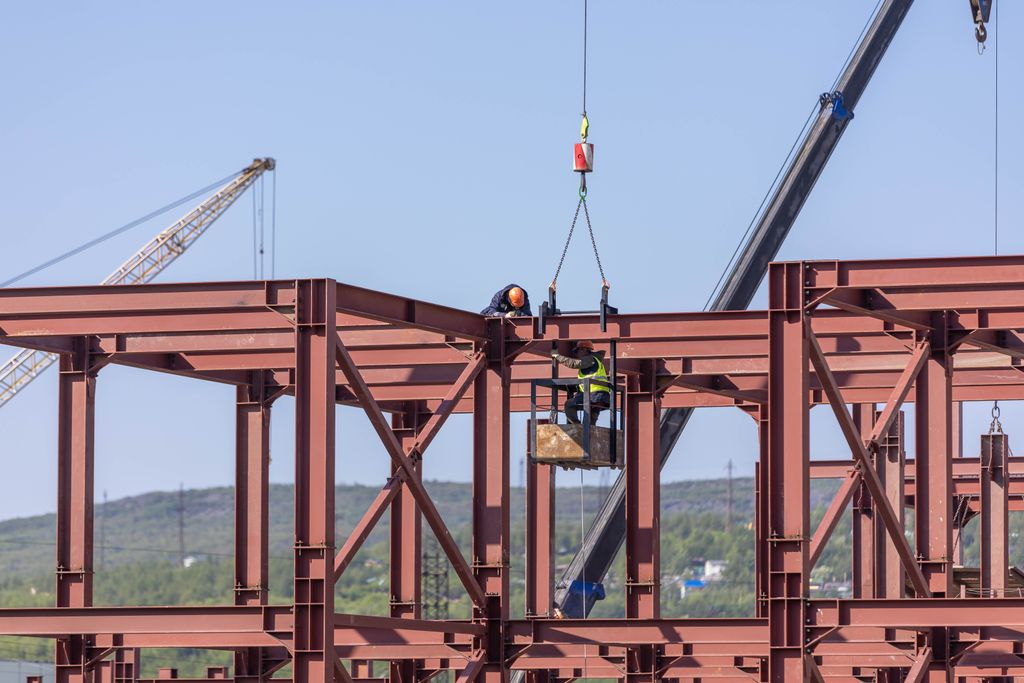 Flambement Construction workers assembling steel frame structure with cranes in daylight outdoors.